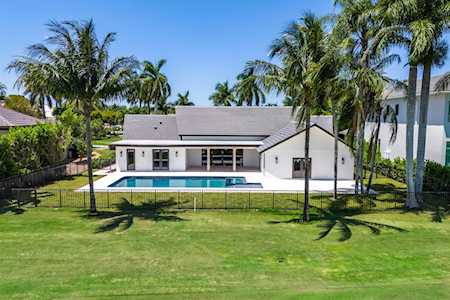 Modern white home with a swimming pool, broad lawn, and palm trees.