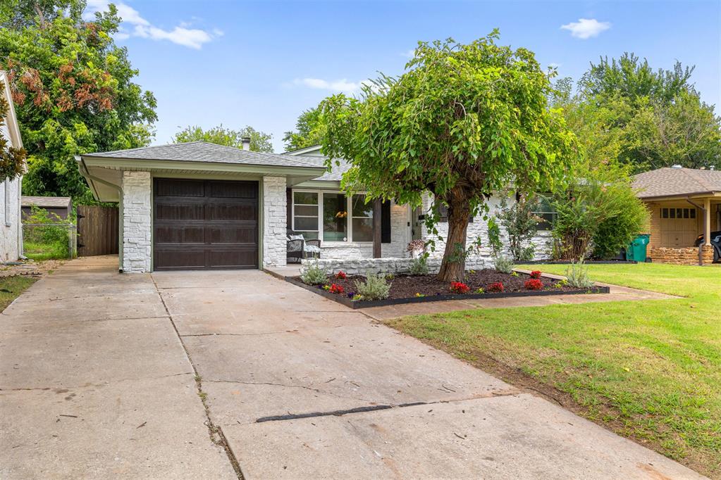 Single-story white stone house with a dark garage door, wide driveway, and landscaped front garden.