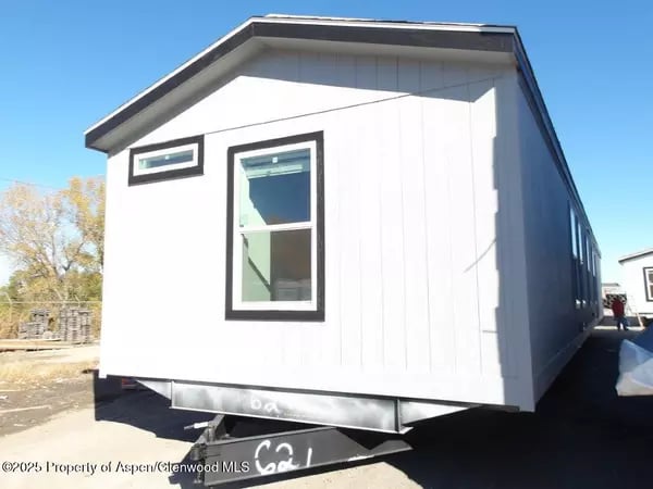White tiny home on a trailer with black-trimmed windows.