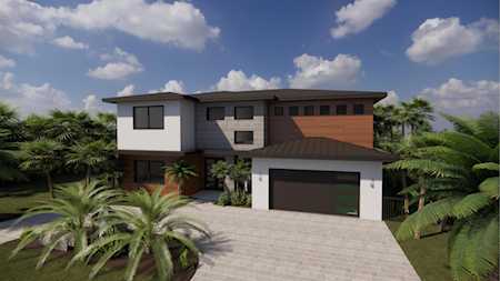 Modern two-story home with a dark double garage door, wide driveway, and tropical landscaping.