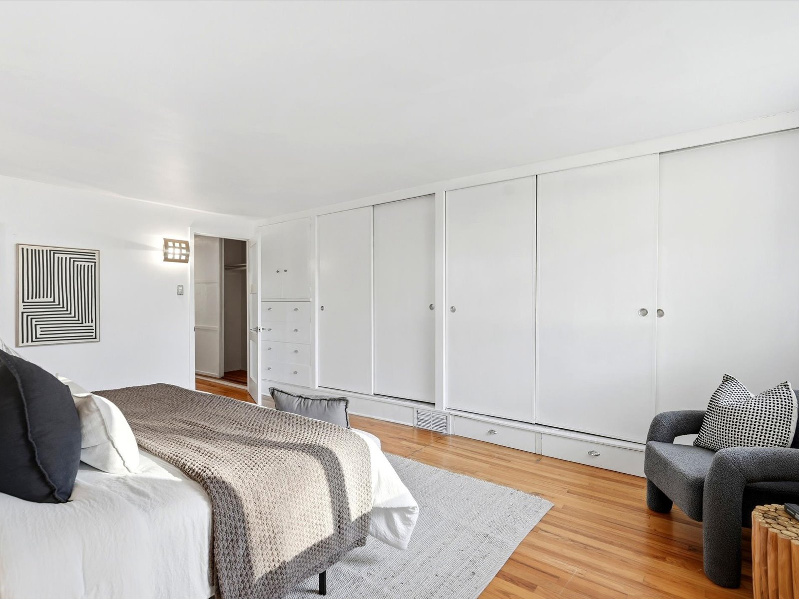 Bedroom with white built-in closets, hardwood floors, and a bed with a textured gray throw.