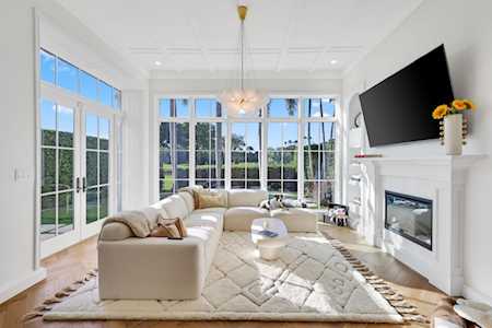 Bright living room with a cream sectional, large windows, and a white fireplace beneath a mounted television.