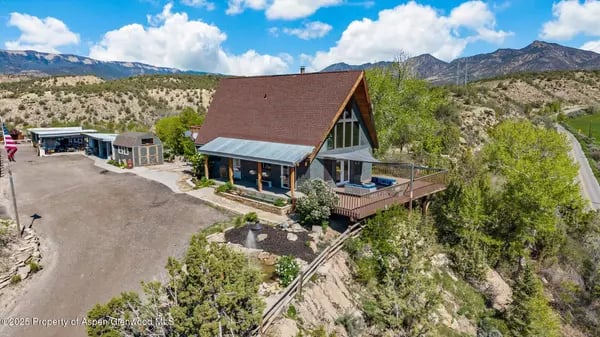 A-frame building with a broad brown roof and deck, surrounded by hills and mountain views.