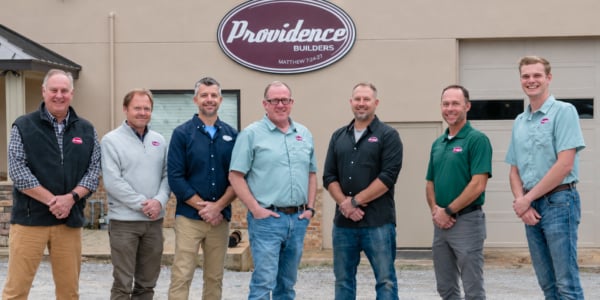 Seven men pose outside beneath a Providence Builders sign.