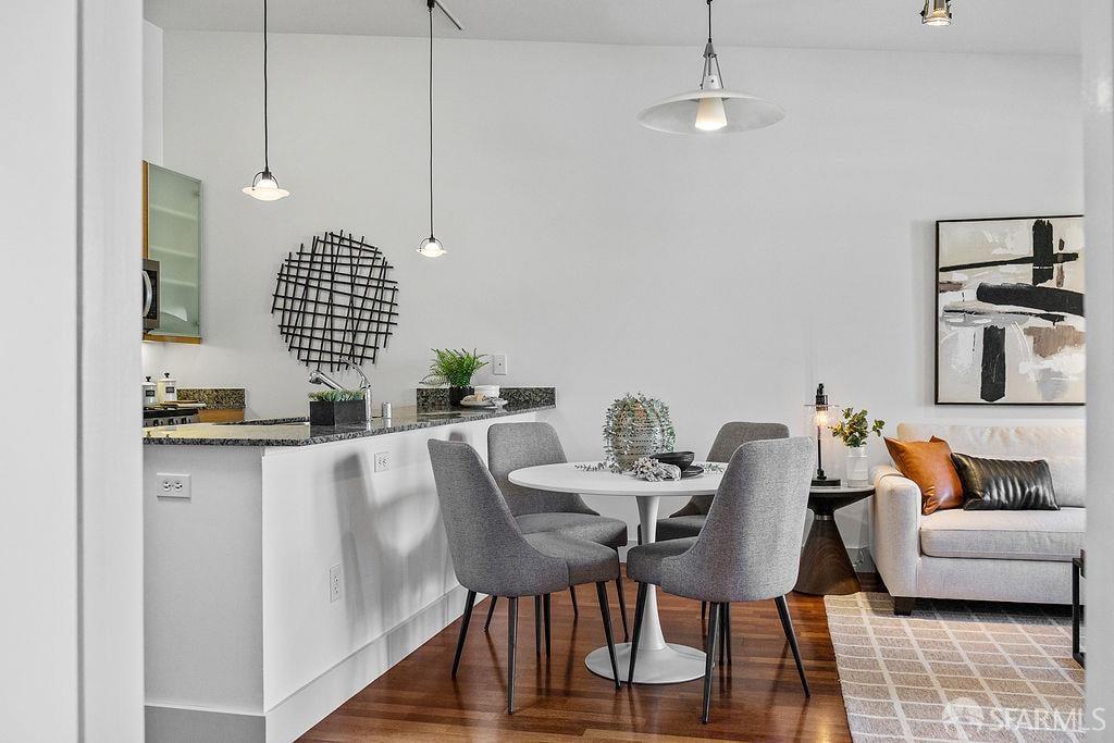Open-plan dining area with gray chairs beside a granite kitchen peninsula and white living room sofa.