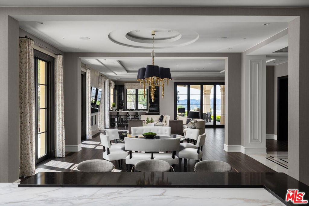 Open-plan living and dining room with white seating, dark floors, and mountain views through large windows.
