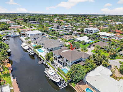 Aerial view of canal-front homes, docks, boats, and pools, with a red arrow marking one house.