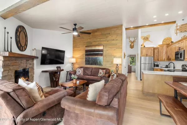Living room with leather sofas, a stone fireplace, and a wood-plank accent wall beside the kitchen.
