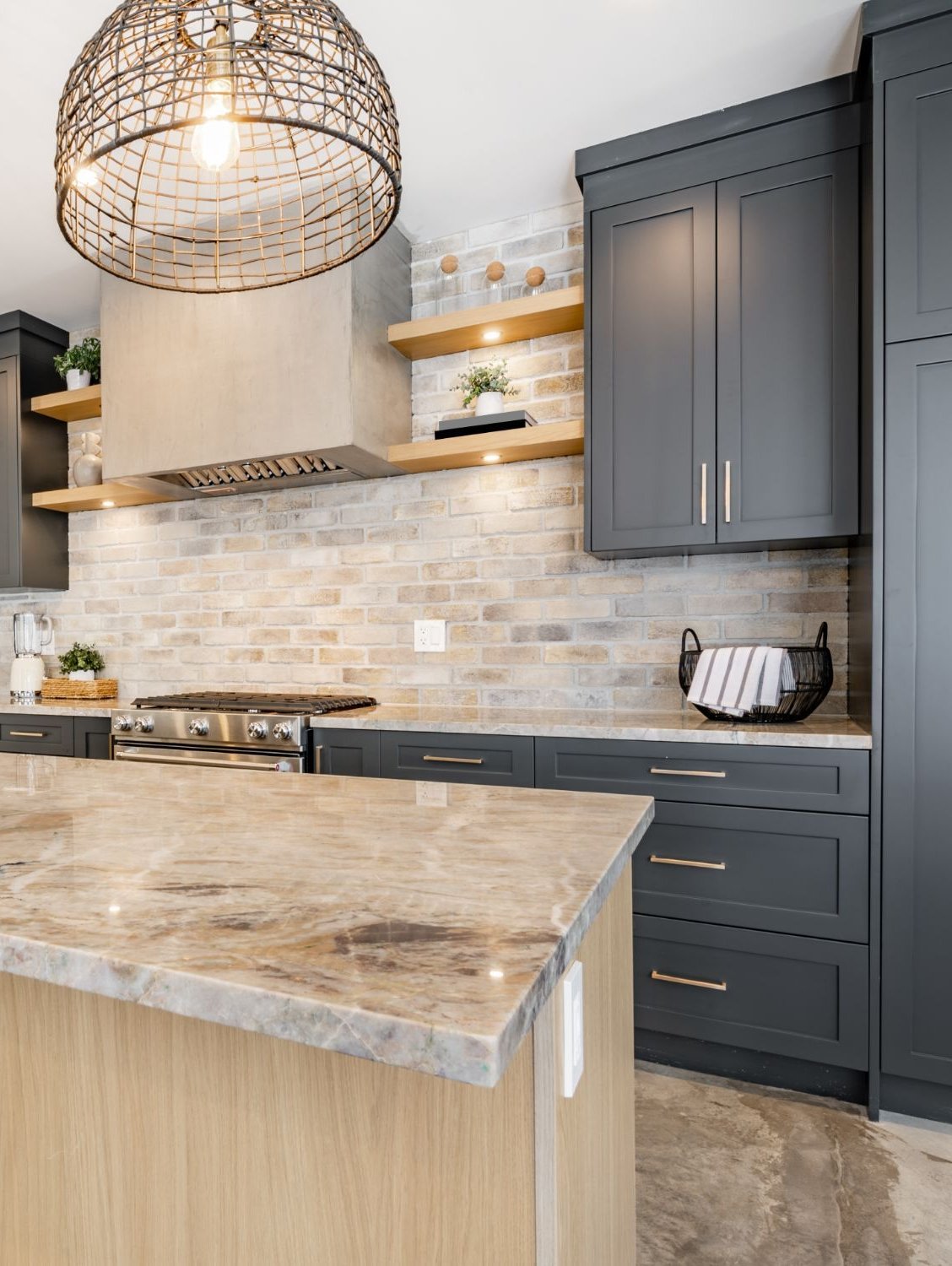 Modern kitchen with charcoal cabinets, pale brick backsplash, and a large marble-patterned island.