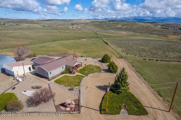 Aerial view of a gray home with a curved driveway amid open rural fields.