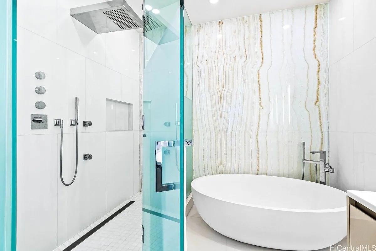 Modern bathroom with a glass shower and freestanding soaking tub against a veined stone wall.