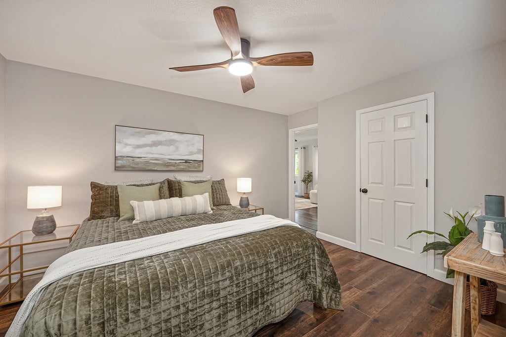 Bedroom with an olive-quilted bed, hardwood floors, and a wood-bladed ceiling fan