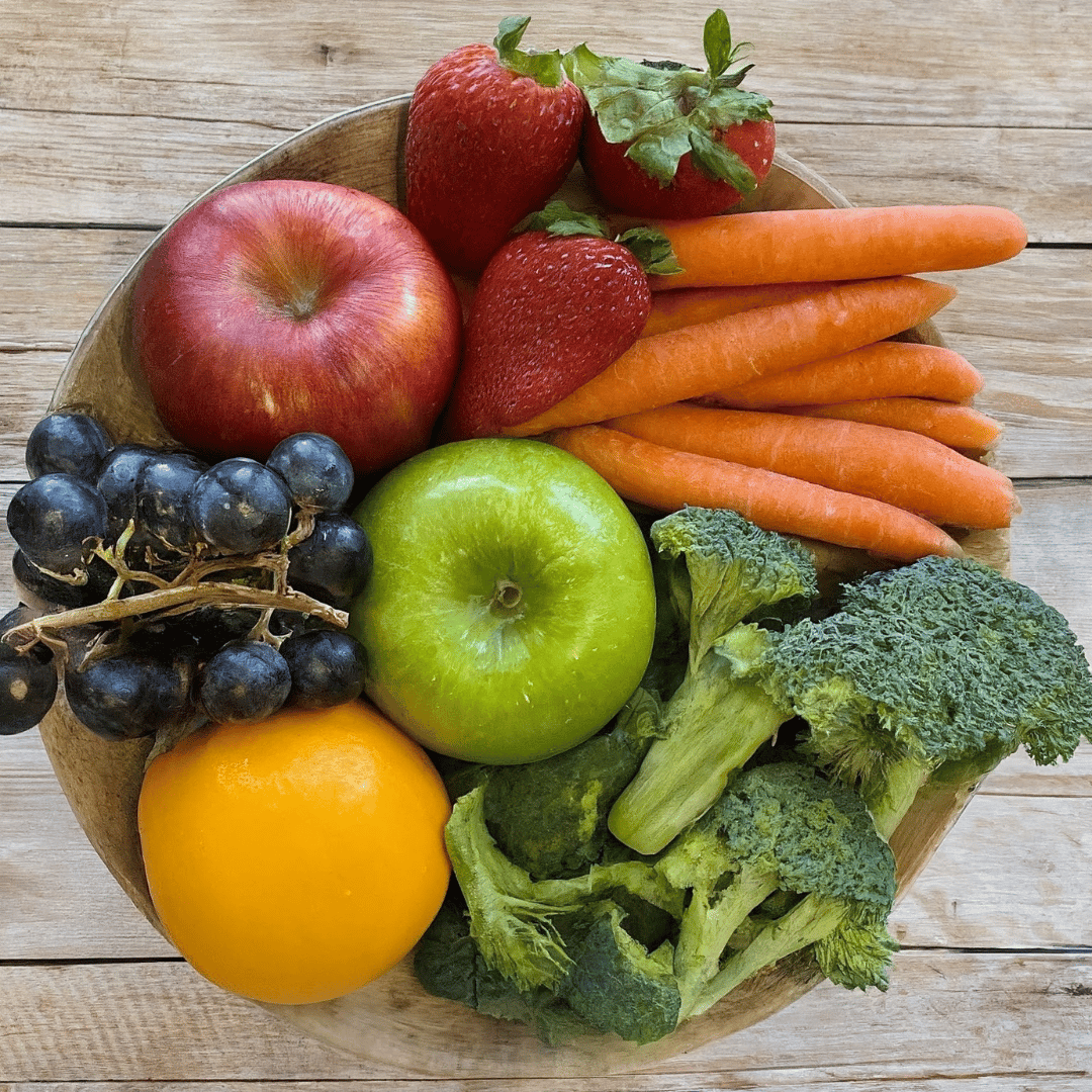Bowl of fresh fruit and vegetables with apples, strawberries, carrots, blueberries, an orange, and broccoli.