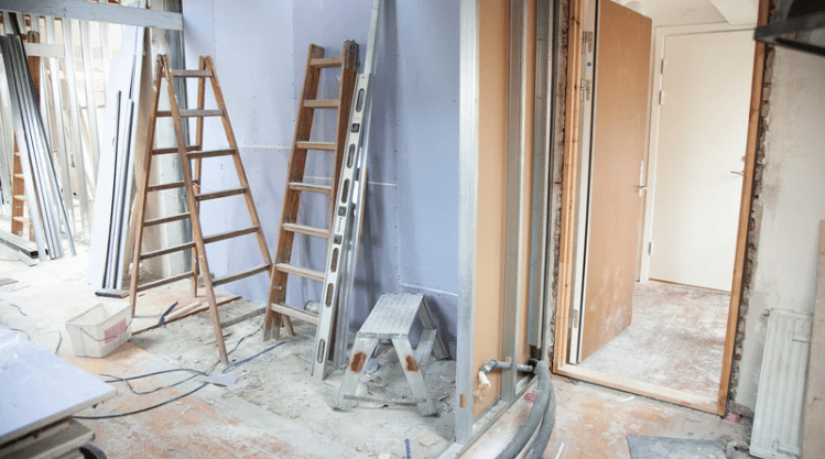 Unfinished interior with ladders, exposed framing, and construction materials on the floor.