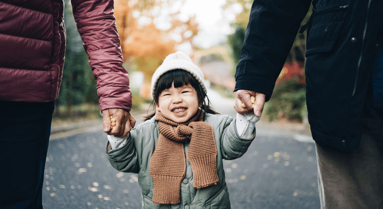 A young girl joyfully holds hands with her parents, symbolizing love and family unity.