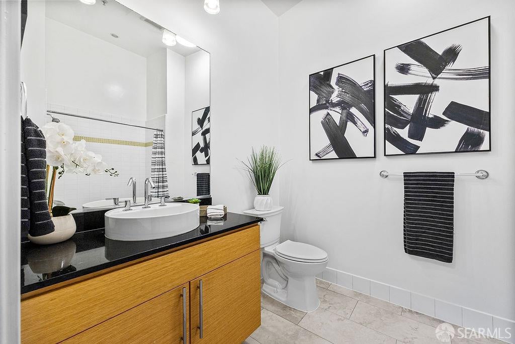 Bathroom with a vessel sink, black countertop, wood vanity, and abstract wall art.