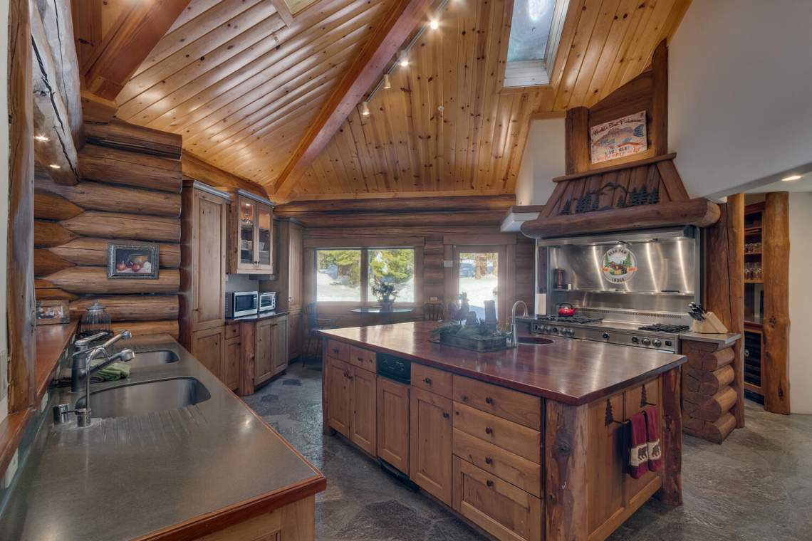 Rustic log-home kitchen with a large wood-topped island, exposed beams, and a stainless-steel range.