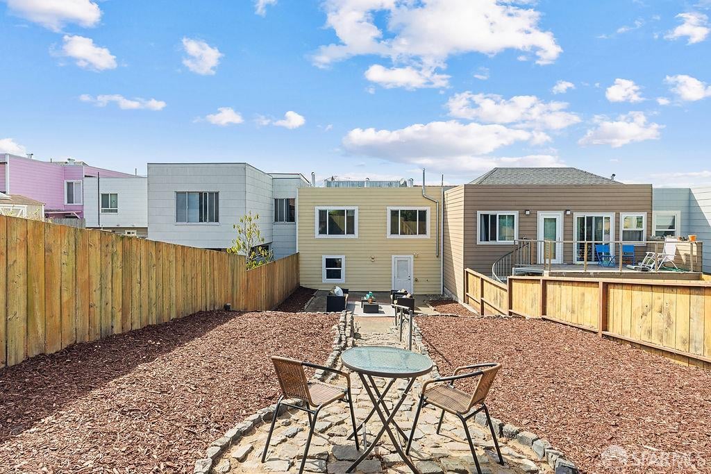 Fenced backyard with wood-chip landscaping, a stone patio, and a raised deck.