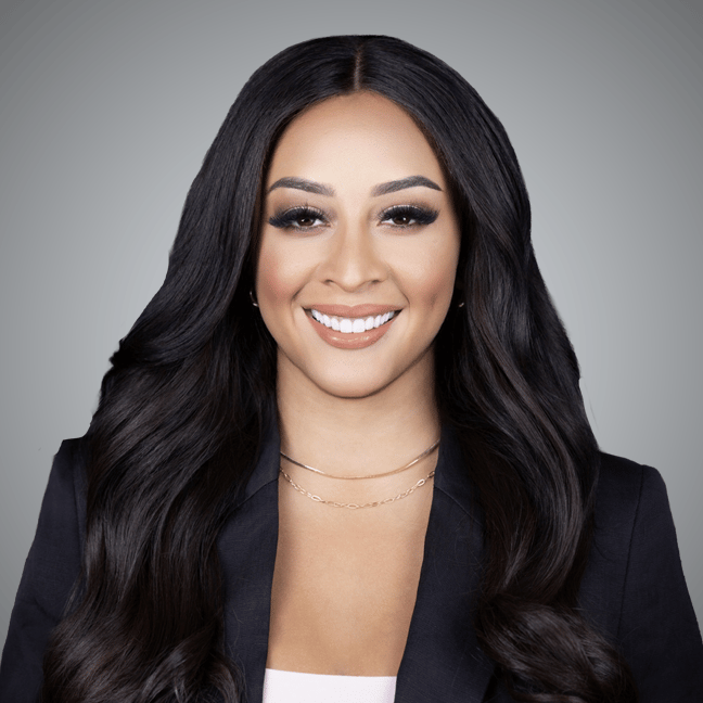 Jasmine Valdez smiling in a dark blazer, with long dark hair and layered gold necklaces.