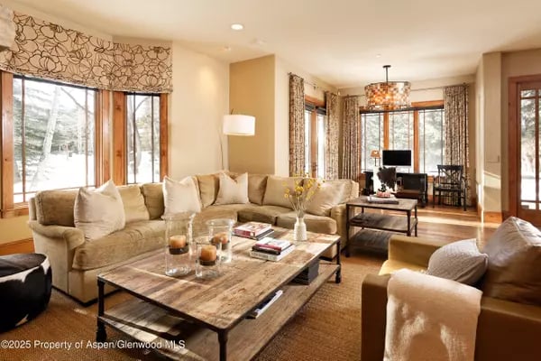 Furnished living room with a beige sectional, rustic coffee table, and tall windows.
