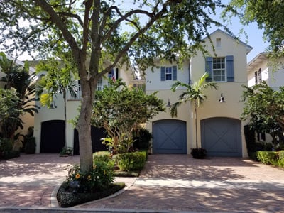 Two-story attached homes with blue-gray garage doors, shaded by a large tree.