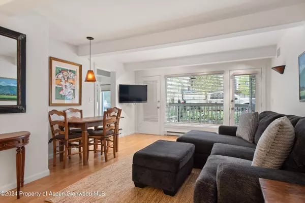 Living room with a dark sectional, ottoman, hardwood floors, and glass doors to a balcony.