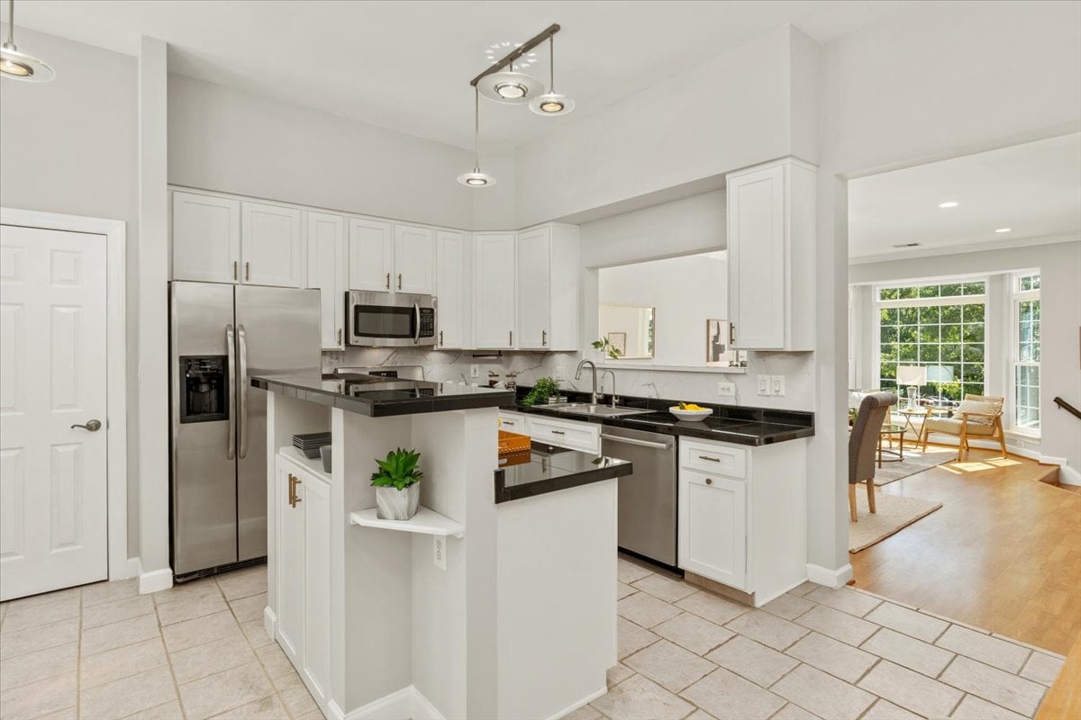 Bright kitchen with white cabinets, black countertops, stainless steel appliances, and a central peninsula.