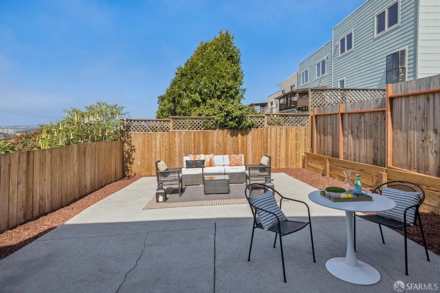 Furnished concrete patio with lounge seating, a dining table, and tall wooden privacy fences.