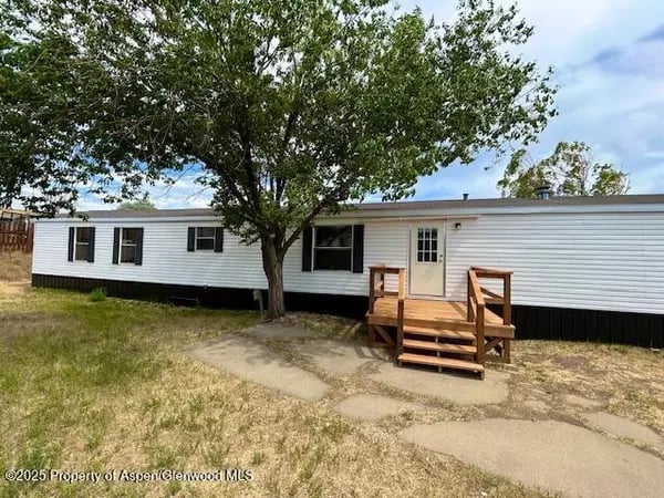 White manufactured home with wooden front steps beneath a large leafy tree.