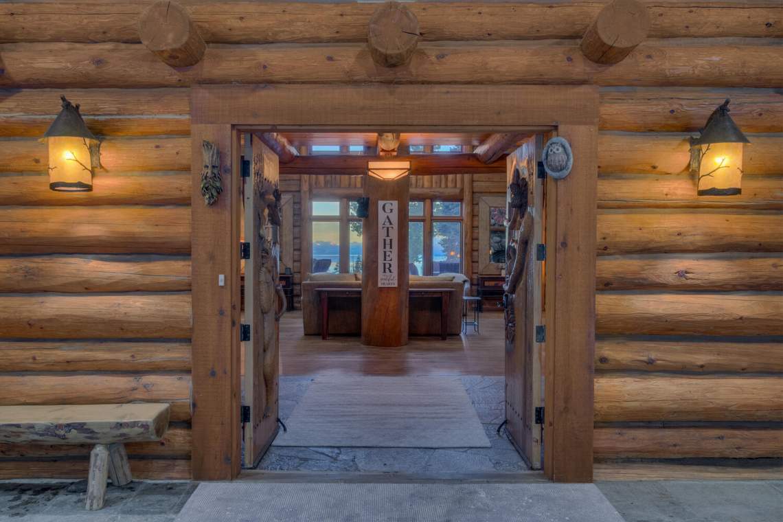 Log-home entryway opens to a gathering room with a lake visible through the windows.