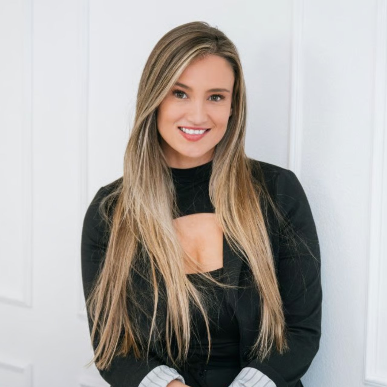 Alyssa Abache, real estate agent, smiling in a black top with long highlighted hair.