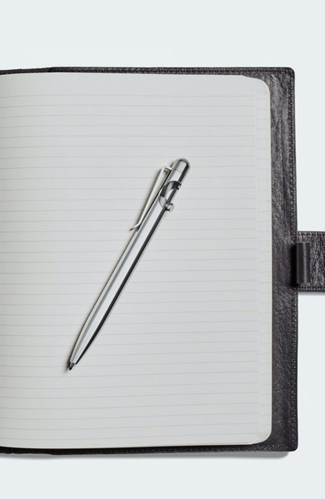 Silver pen resting diagonally on the lined pages of an open notebook.