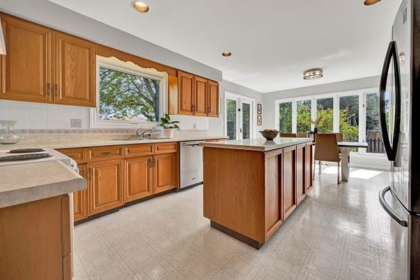 Kitchen with wood cabinets, a large island, and windows overlooking a leafy yard.