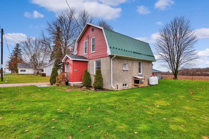 Rural two-story home with red upper siding, gray stone lower level, and green metal roof.