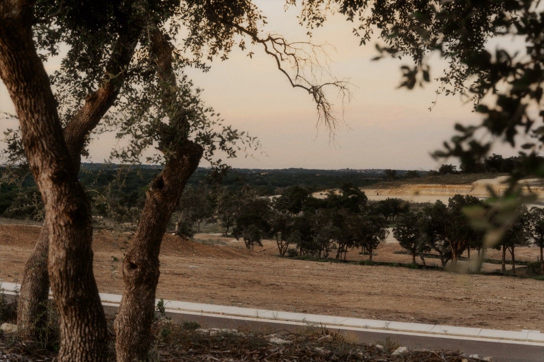 Vacant homesite with oak trees, a roadside frontage, and wooded hills in the distance.
