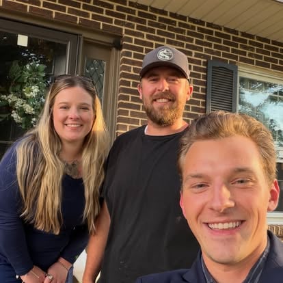 Aaron with clients outside a brick home