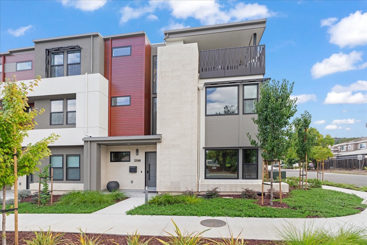 Modern townhome with red siding, an upper balcony, and a landscaped front lawn.