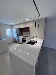 Modern white kitchen with a large island, black faucet, cooktop, and stainless steel appliances.