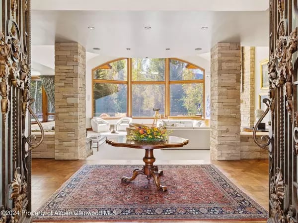 Living room with an arched picture window, stone columns, carved woodwork, and a floral centerpiece.