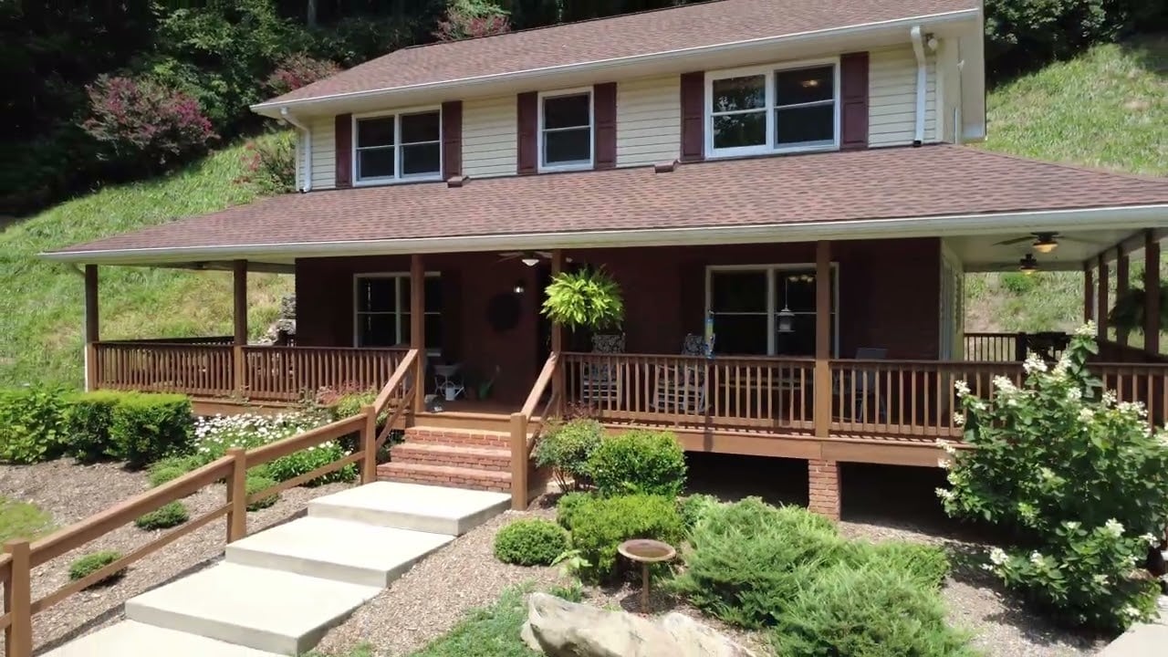 Hillside home with a broad covered porch, wooden railings, and landscaped front garden.