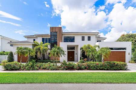 Modern white home with a wood-accented entry, palm trees, and landscaped front yard.