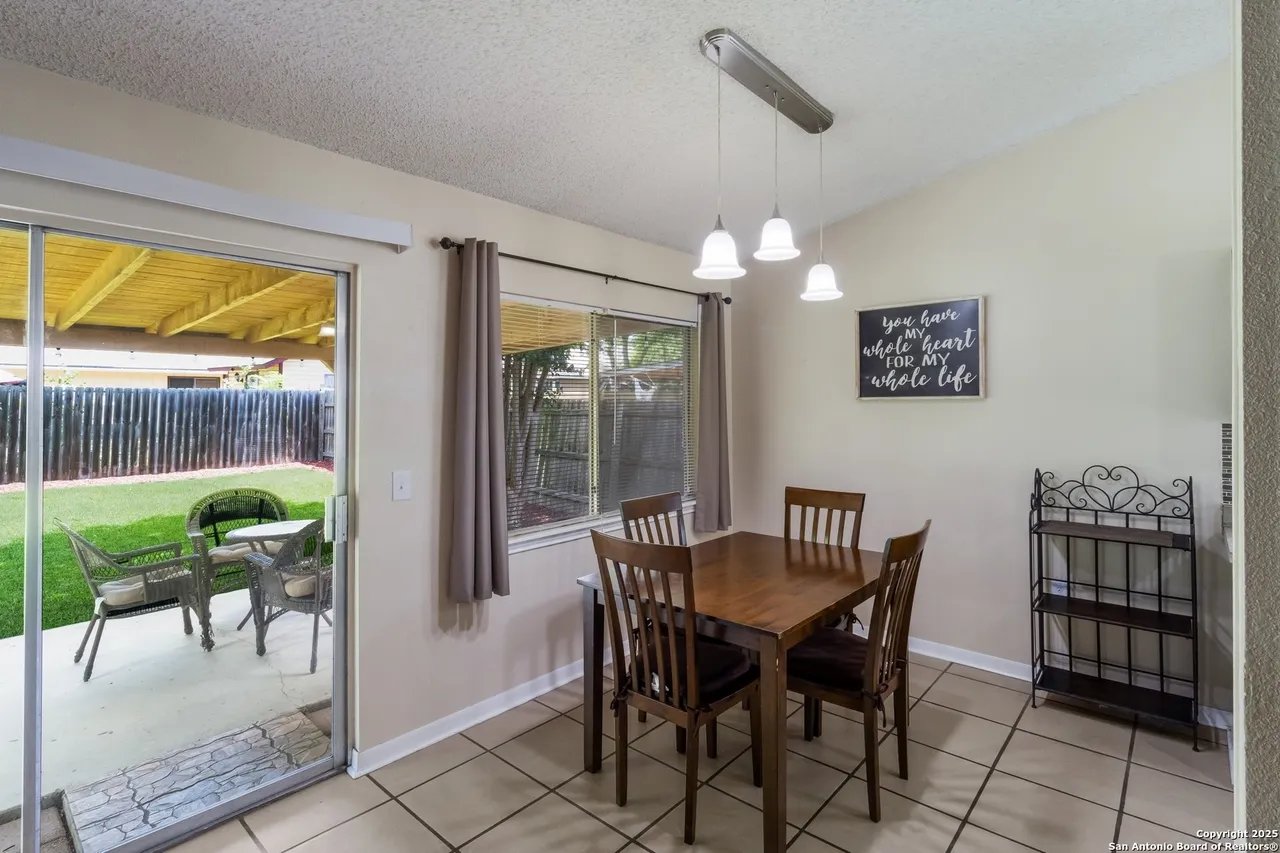 Dining area with a wood table and chairs beside a sliding glass door opening onto a covered patio.