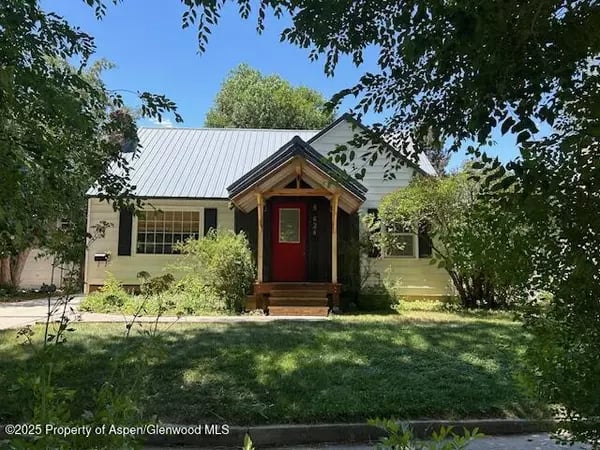 House with a red front door and peaked entry porch, framed by mature trees.