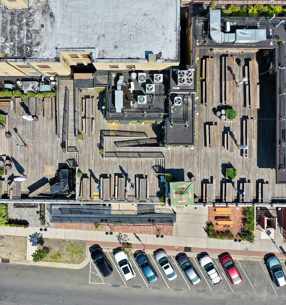Aerial view of a rooftop deck with wooden seating, planters, and rooftop equipment.