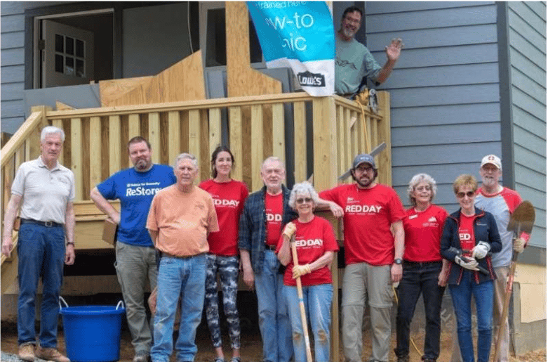 Volunteers pose outside a home under construction, several wearing red Red Day shirts.