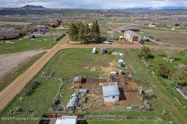 Rural property with a small house, outbuildings, fenced grounds, and distant mountains.