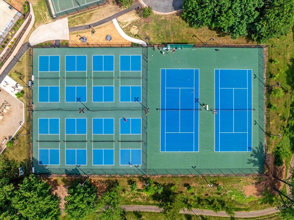 Aerial view of blue pickleball and tennis courts surrounded by trees.