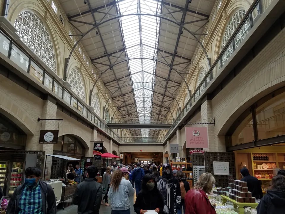 Shoppers walking through the Ferry Building Marketplace nave past signs for Miette P&acirc;tisserie and The Epicurean Trader.