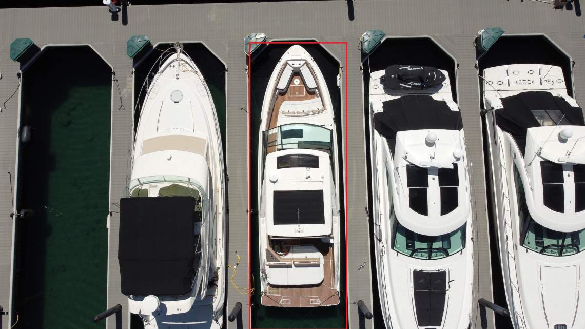 White motor yacht with a tan deck docked between other boats, outlined in red.