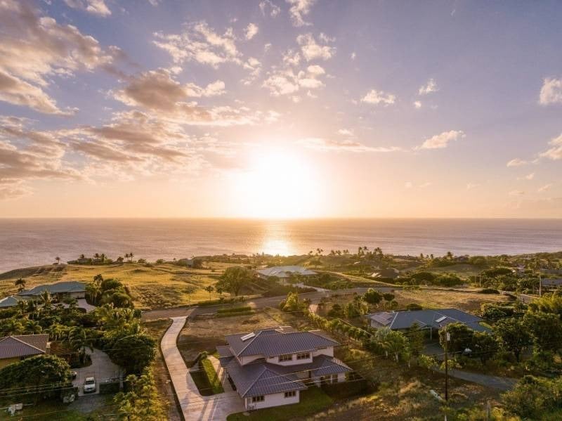 Two-story home amid tropical greenery, with the Pacific Ocean and sunset beyond.
